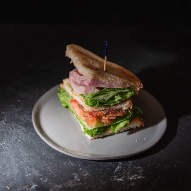 Clubsandwich met ham, tomaat en sla op een grijs bord