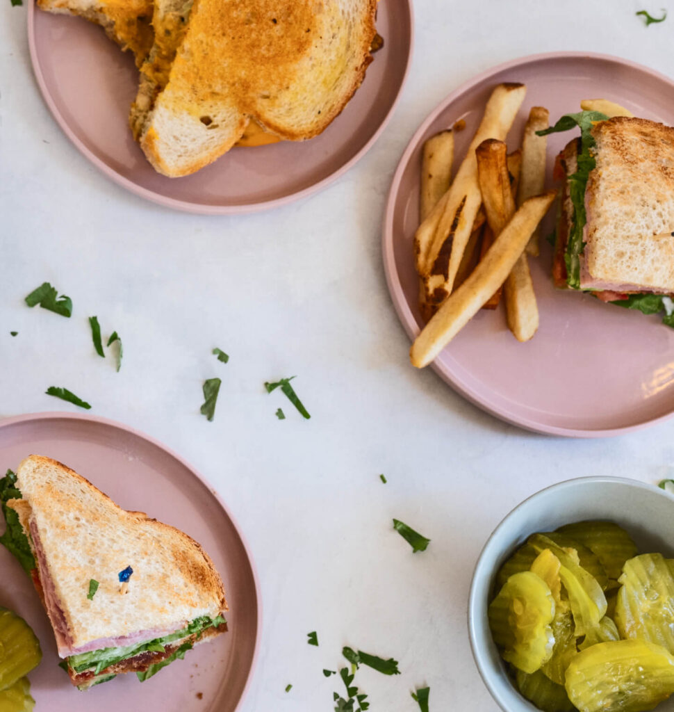 Getoaste sandwiches op roze borden, met friet en een schaaltje augurken