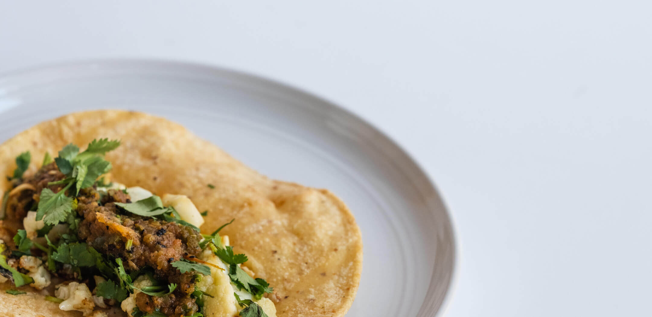 Gevulde tortilla met bloemkool en verse koriander op een wit bord