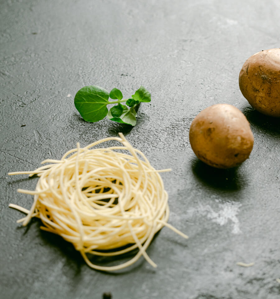 Nestje verse pasta met twee aardappels en verse blaadjes op een donkere stenen ondergrond